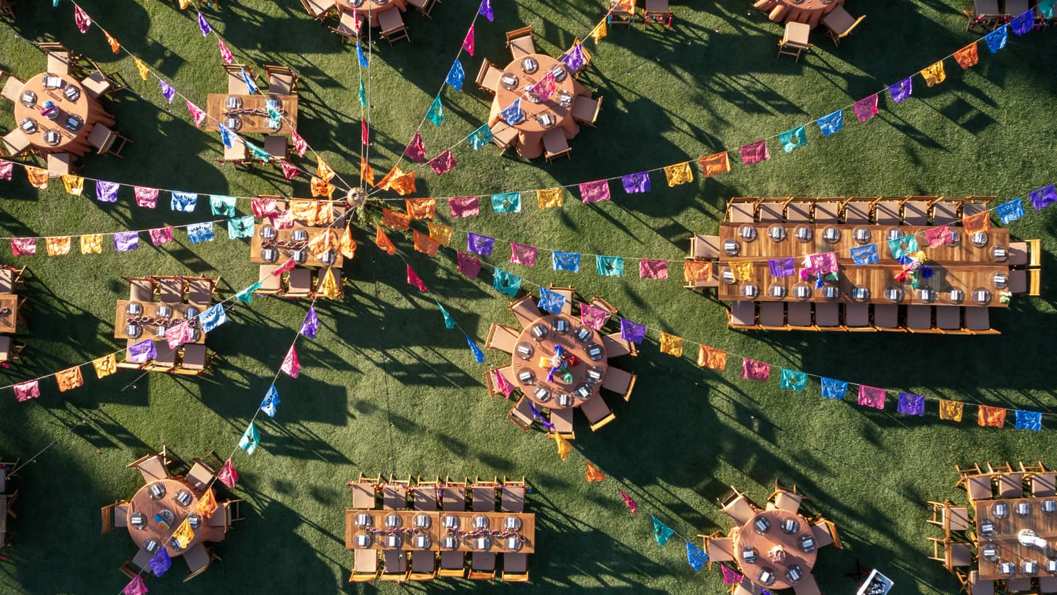 Many dining tables and chairs set up with colourful streamer decorations above it.