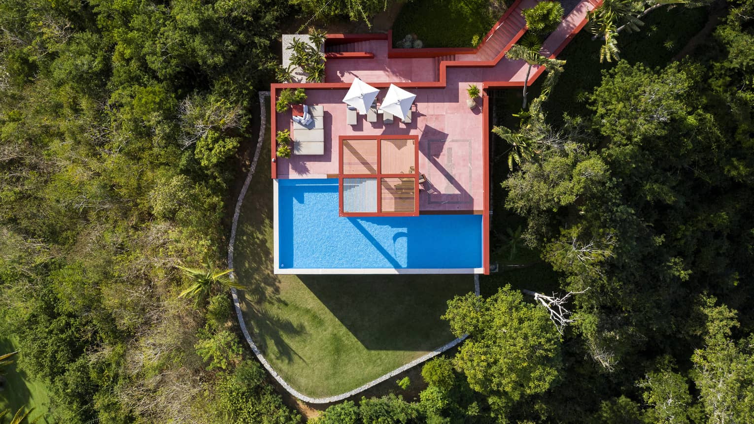 Aerial view of red villa nestled in the jungle with a pool and pool deck
