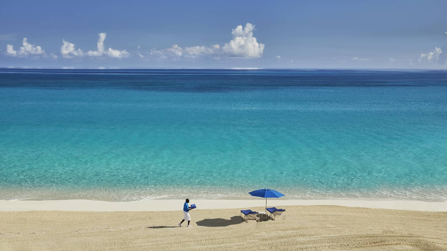 View over ocean, sand beach where hotel staff carries towels to beach chairs