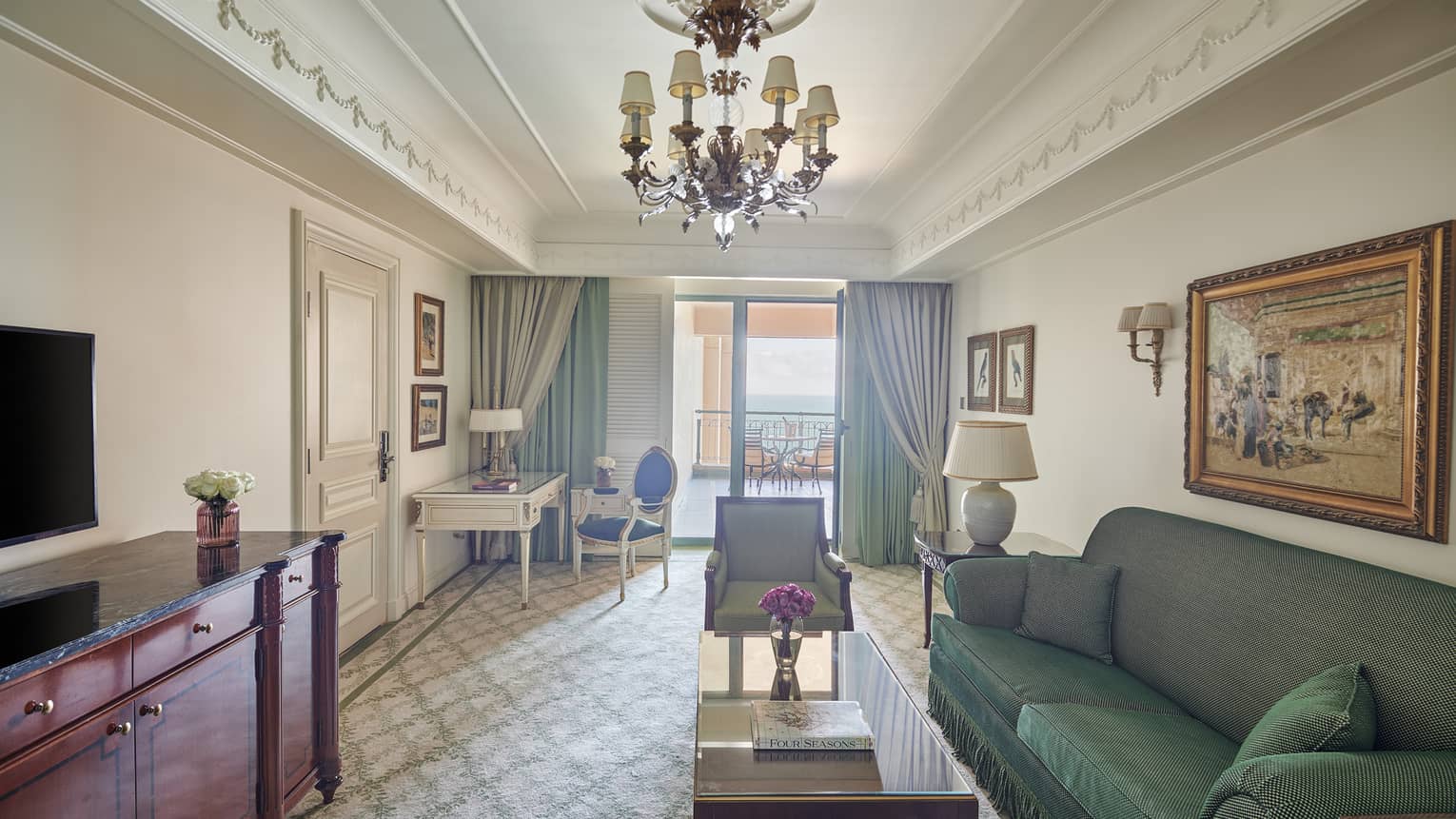 Four Seasons Suite living area with green sofa, twin armchairs, corner desk and chair, glass door to veranda