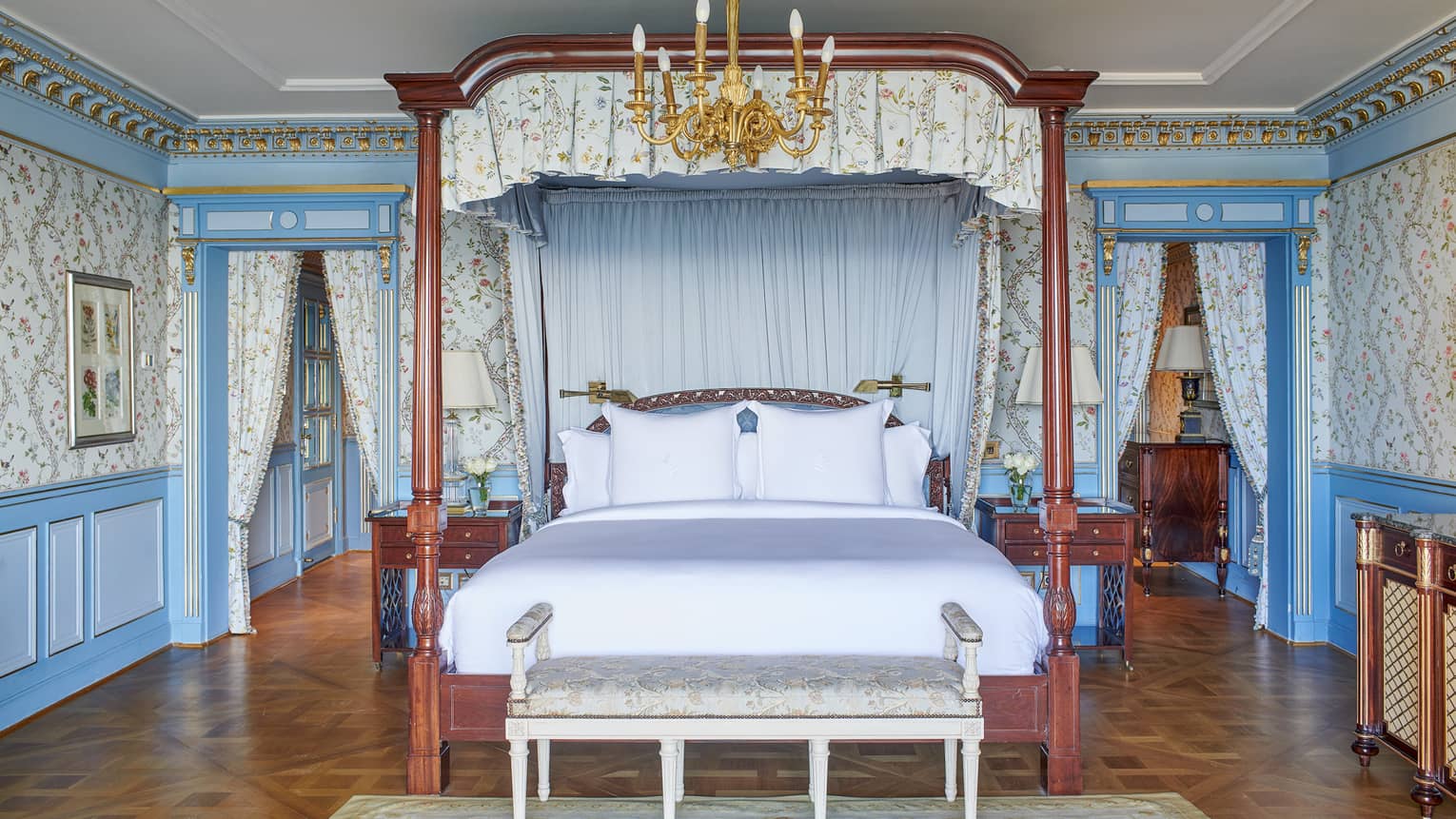 Presidential Suite bedroom with four-poster king bed, blue wall accents, paisley wallpaper, chandelier, parquet flooring