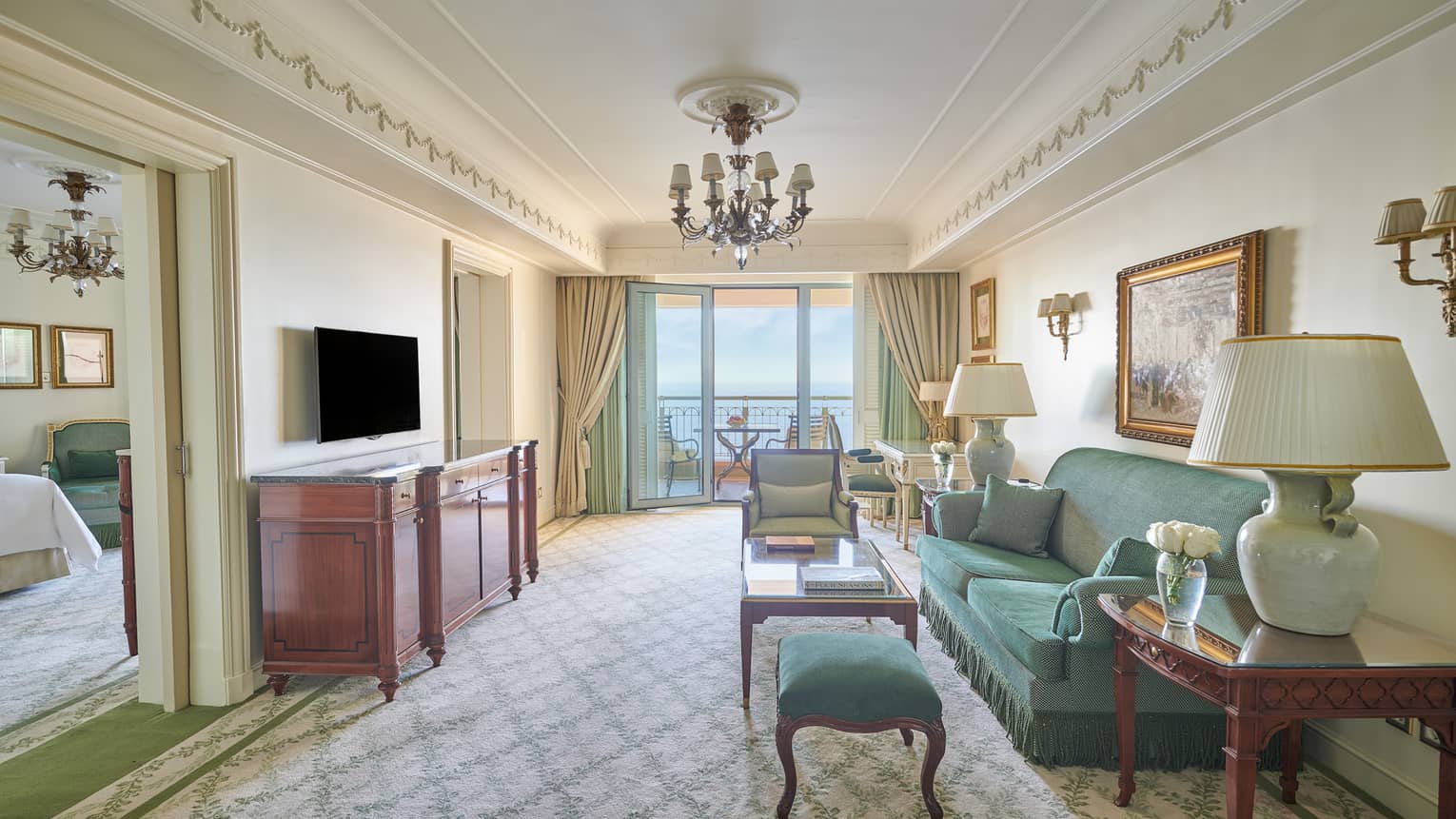 Sea View Suite living area with green sofa, armchair, side tables with lamps, glass door to veranda, bedroom visible through doorway