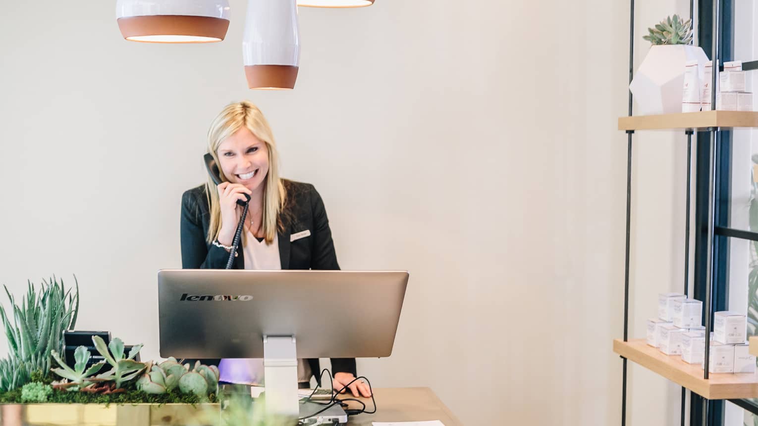 Smiling spa staff on telephone behind large silver computer screen