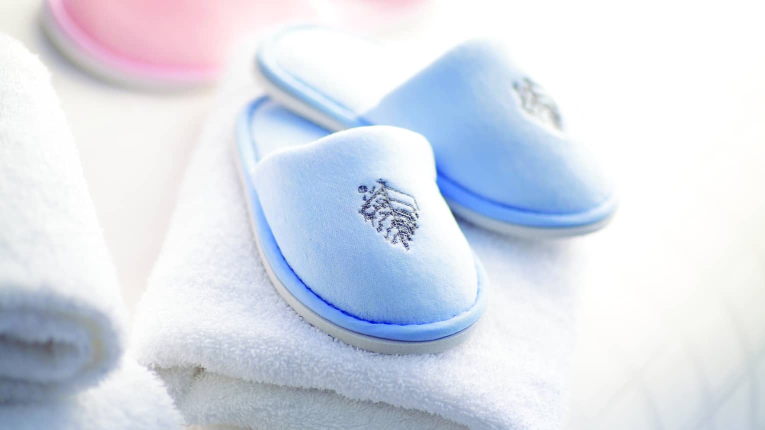 A pair of baby pink and baby blue kid's spa slippers and fluffy white towels