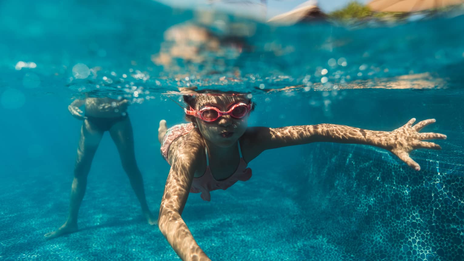 A young boy snorkeling in a pool with red goggles on.
