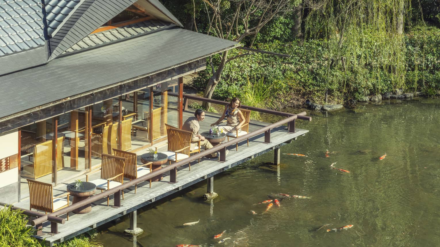 Two people sitting on an outdoor deck overlooking a pond with koi fish at Four Seasons