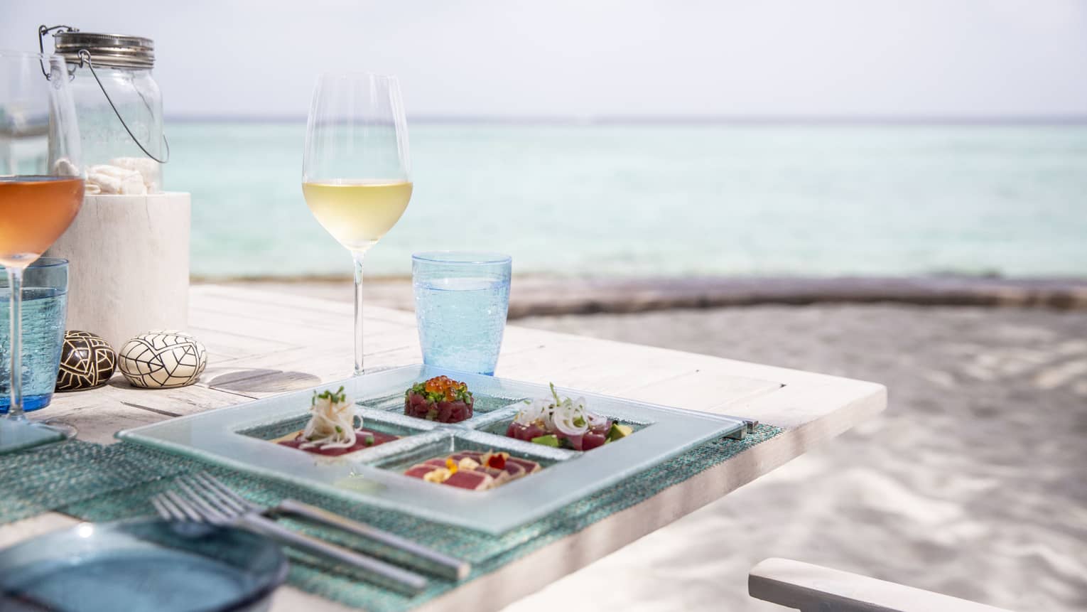 A tasetfully set table with a glass of white wine and rose overlooking the ocean at Fuego Grill