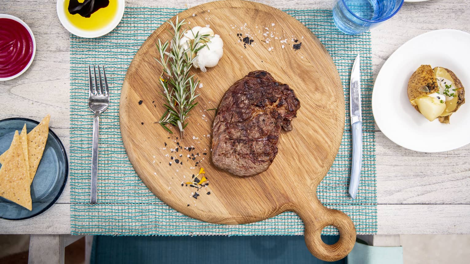 An aerial view of a table with a wooden board with a beef dish and garlic and rosemary at Fuego Grill