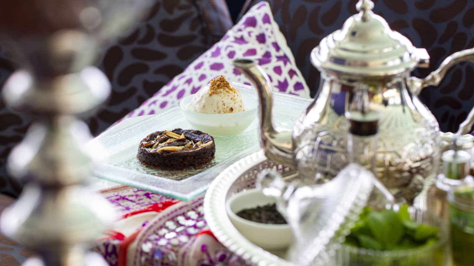 A sterling silver teapot and light tea time finger foods sit on a decorative table spread atAl Barakat