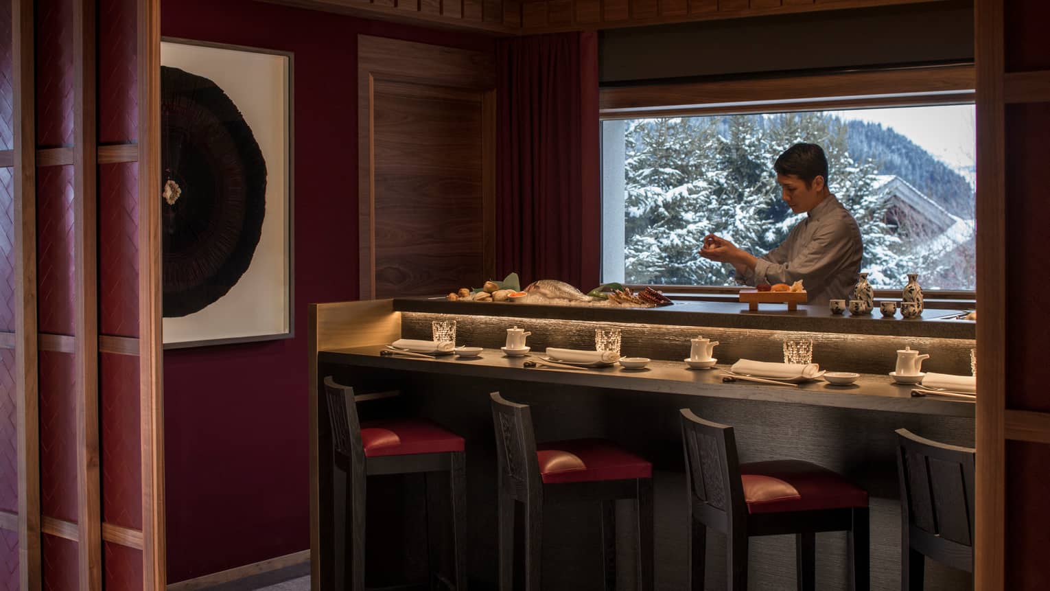 Kaito sushi chef at small bar with fresh whole fish, seafood, window with winter mountain views