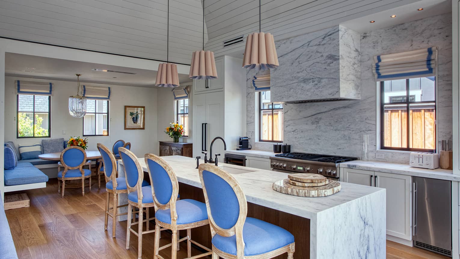 Kitchen with marble island and wall, wooden floors, four blue counter chairs