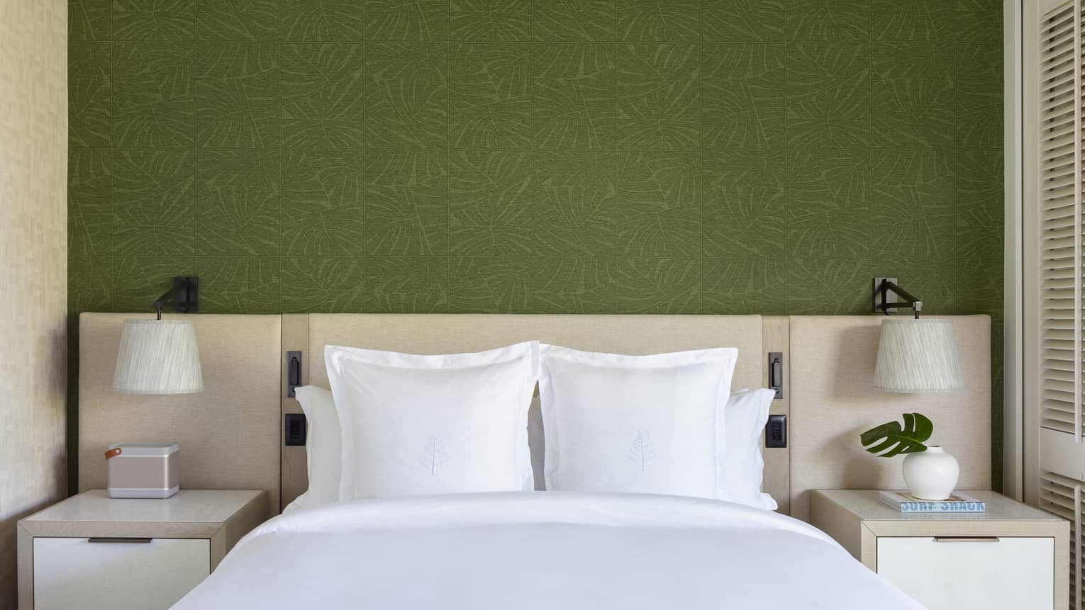 King bed with white sheets and Four Seasons logo on the pillows, set against green wallpaper