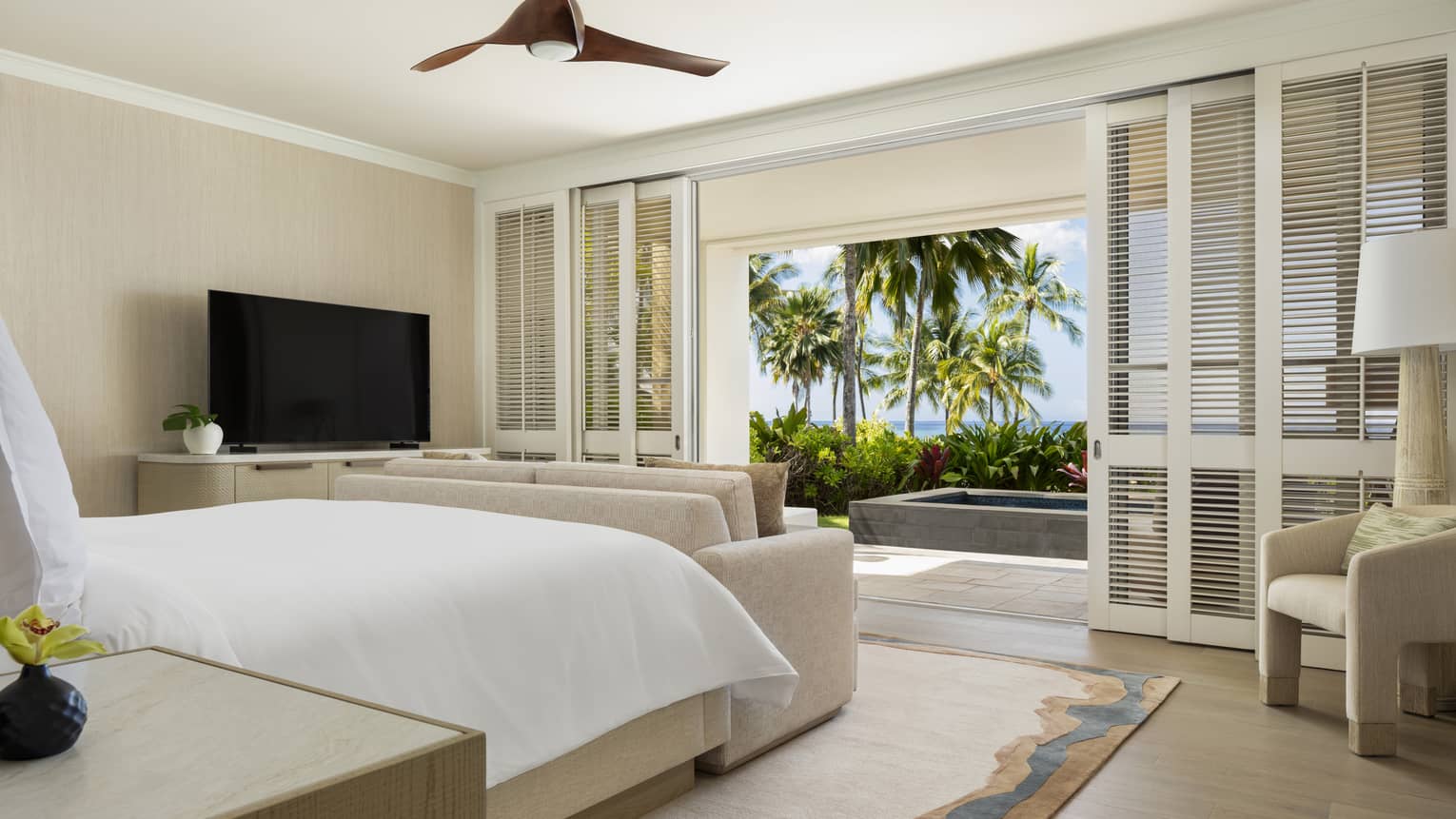 Luxury resort suite bedroom featuring a king bed facing shuttered sliding doors with walk-out ocean-view terrace