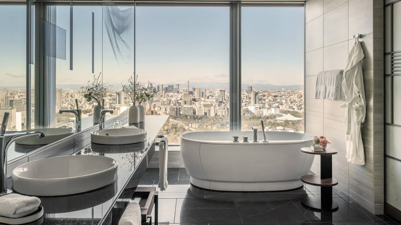 Large hotel suite bathroom with wall of window overlooking city, and a free-standing tub