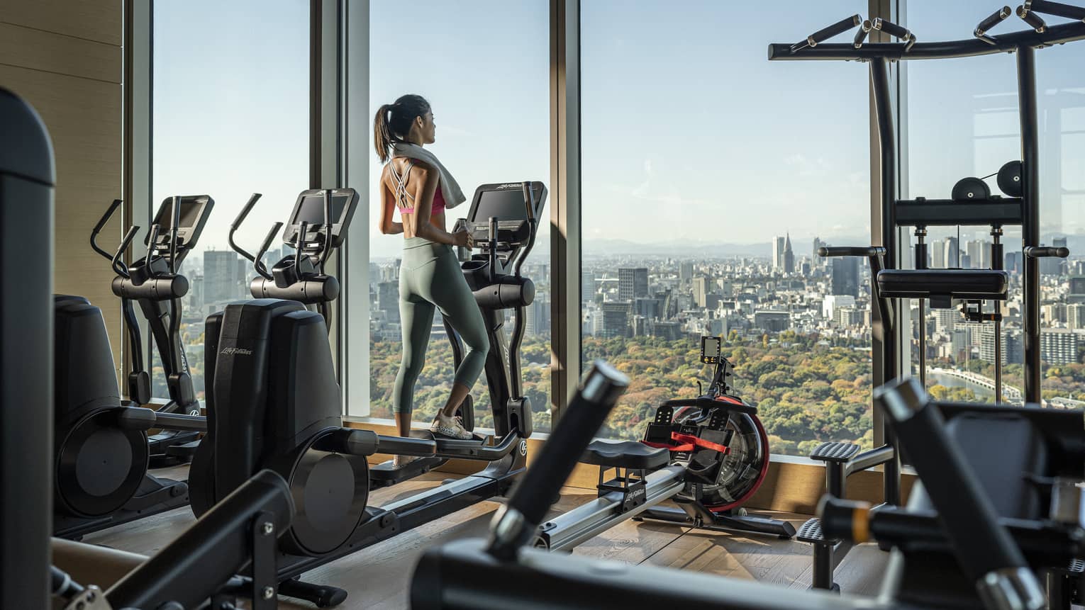 Woman on treadmill gazes out floor-to-ceiling windows of the fitness centre