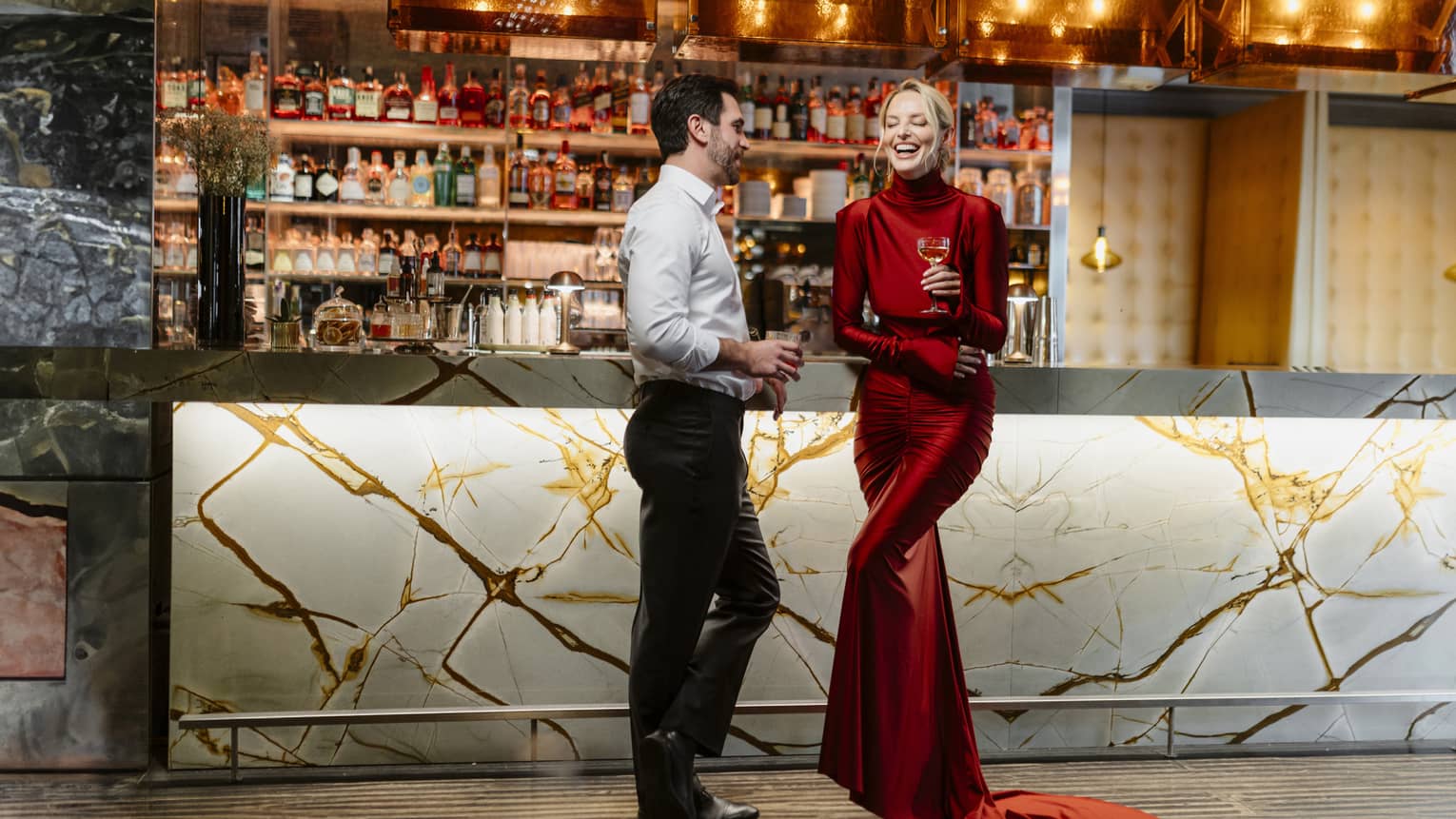 Couple standing, laughing in front of a dimly lit stocked bar