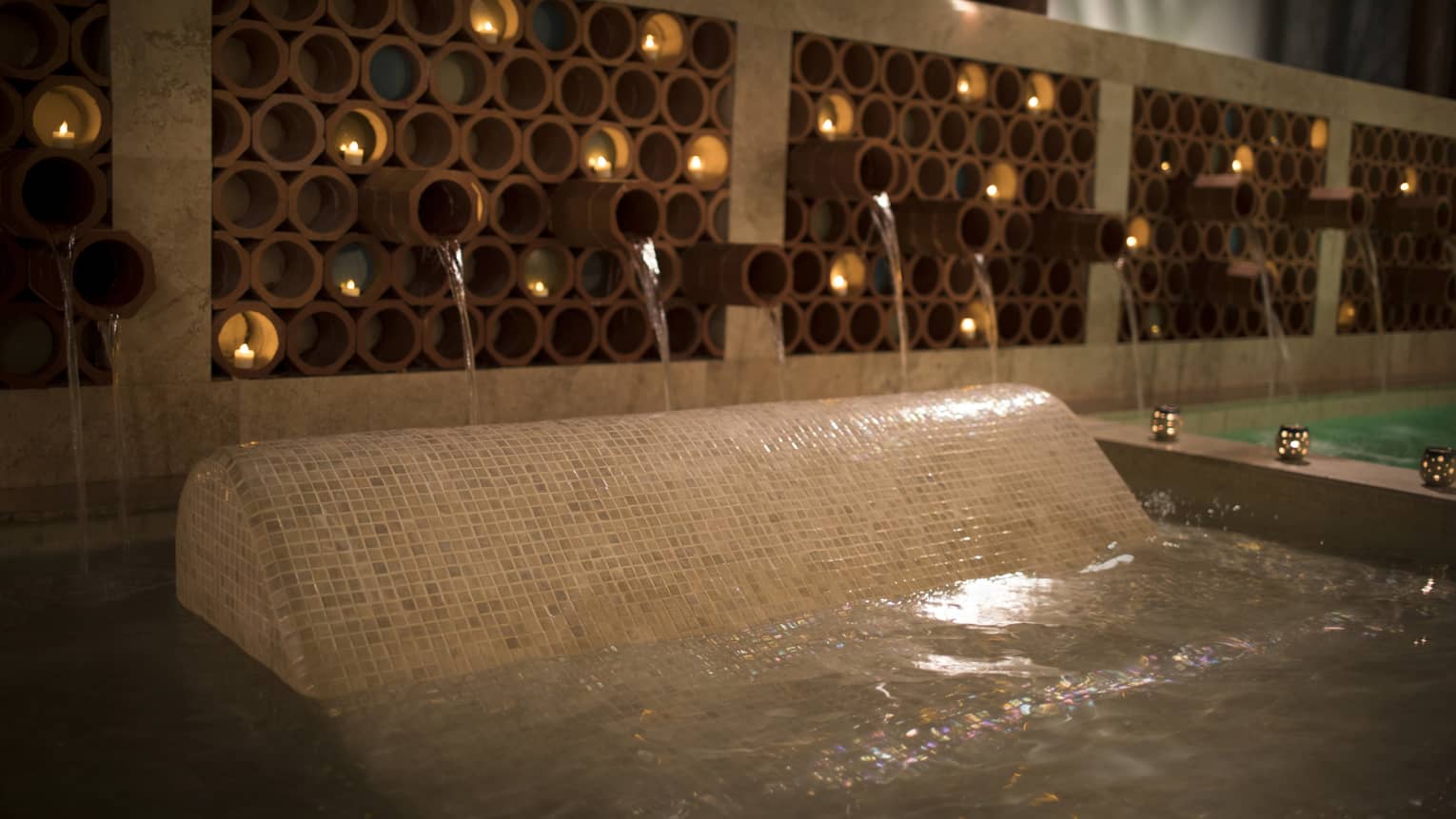 Glowing tea lights in round terracotta vessels over Apuane Spa pools
