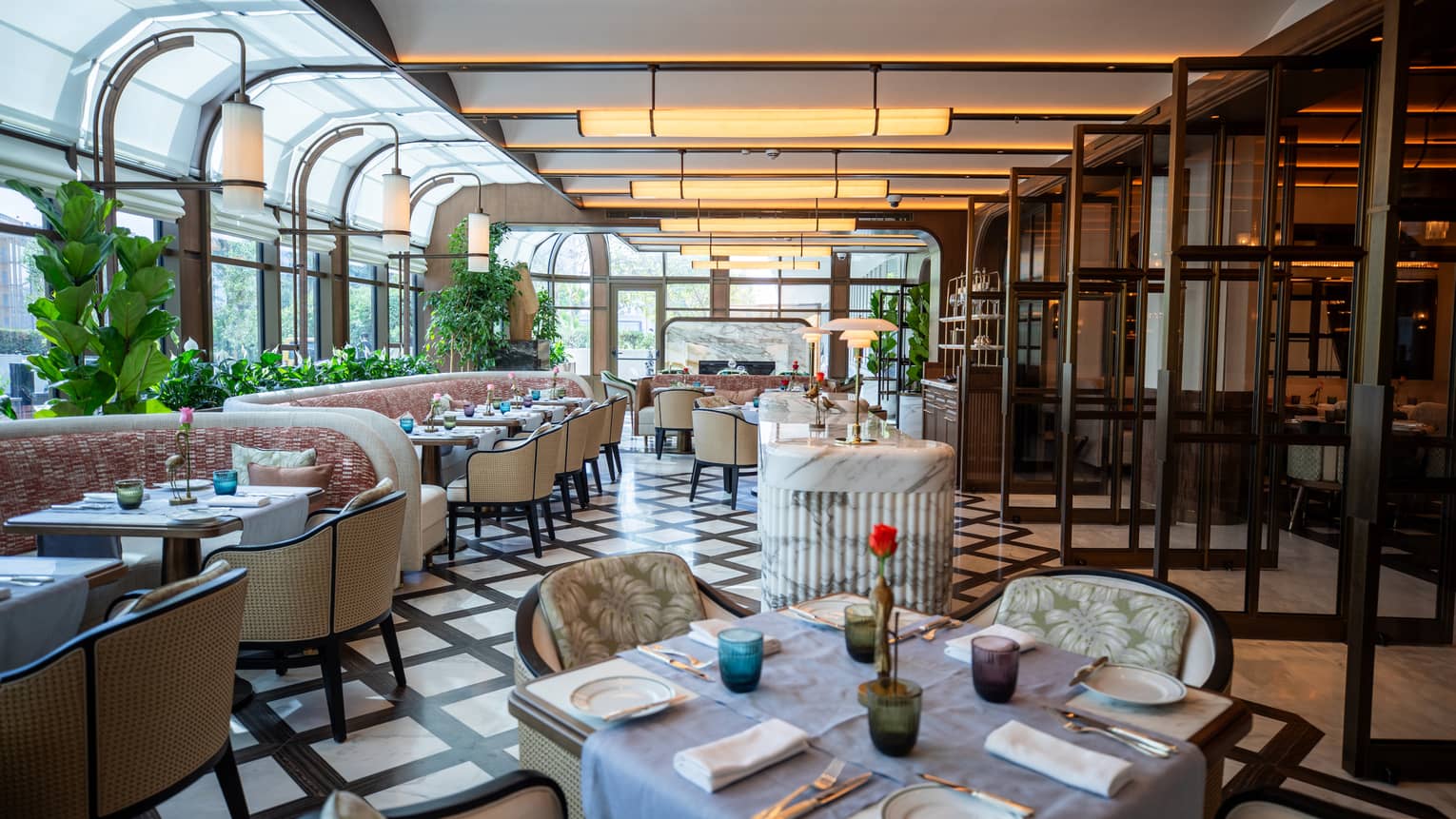 Indoor restaurant with tables of four and booths, black and white tiled floor, plants and overhead lighting