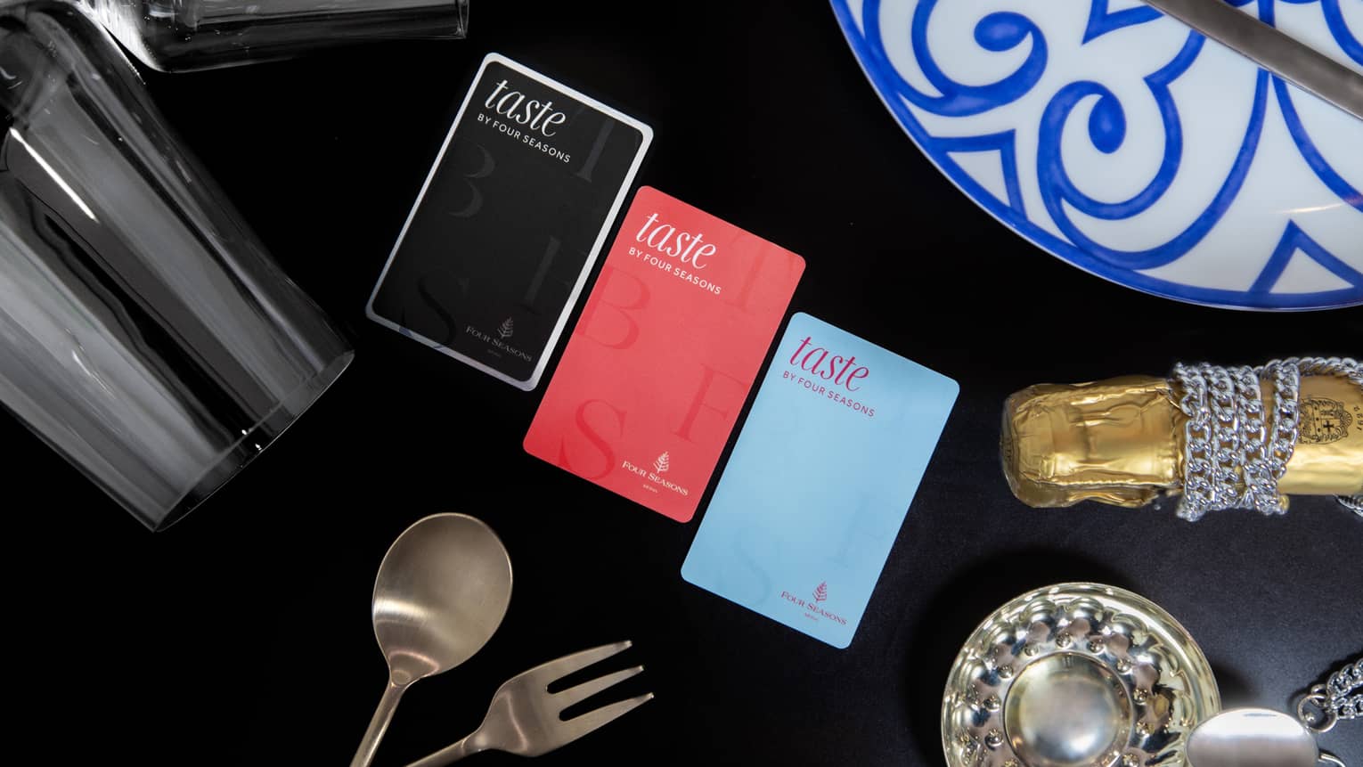 Three colours of Taste by Four Seasons cards on table with black tablecloth, stemmed wine glasses and silver cutlery