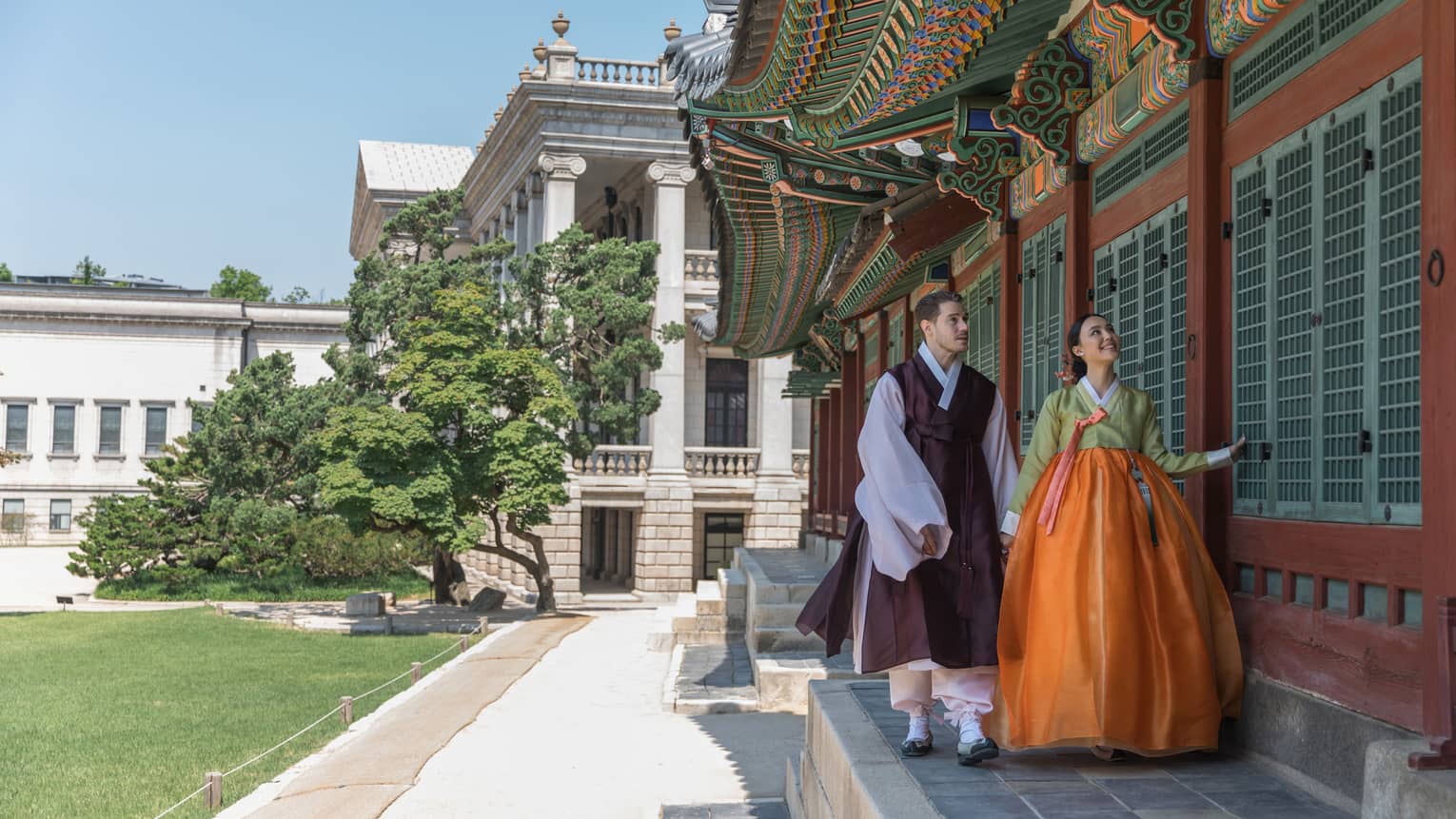 Man and woman in traditional Korean attire walk along the wall of a local palace