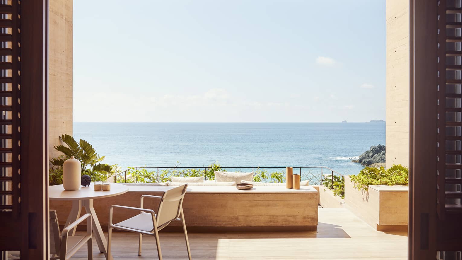 The exterior of a beachfront room with a small table and a large opening looking out at an ocean.