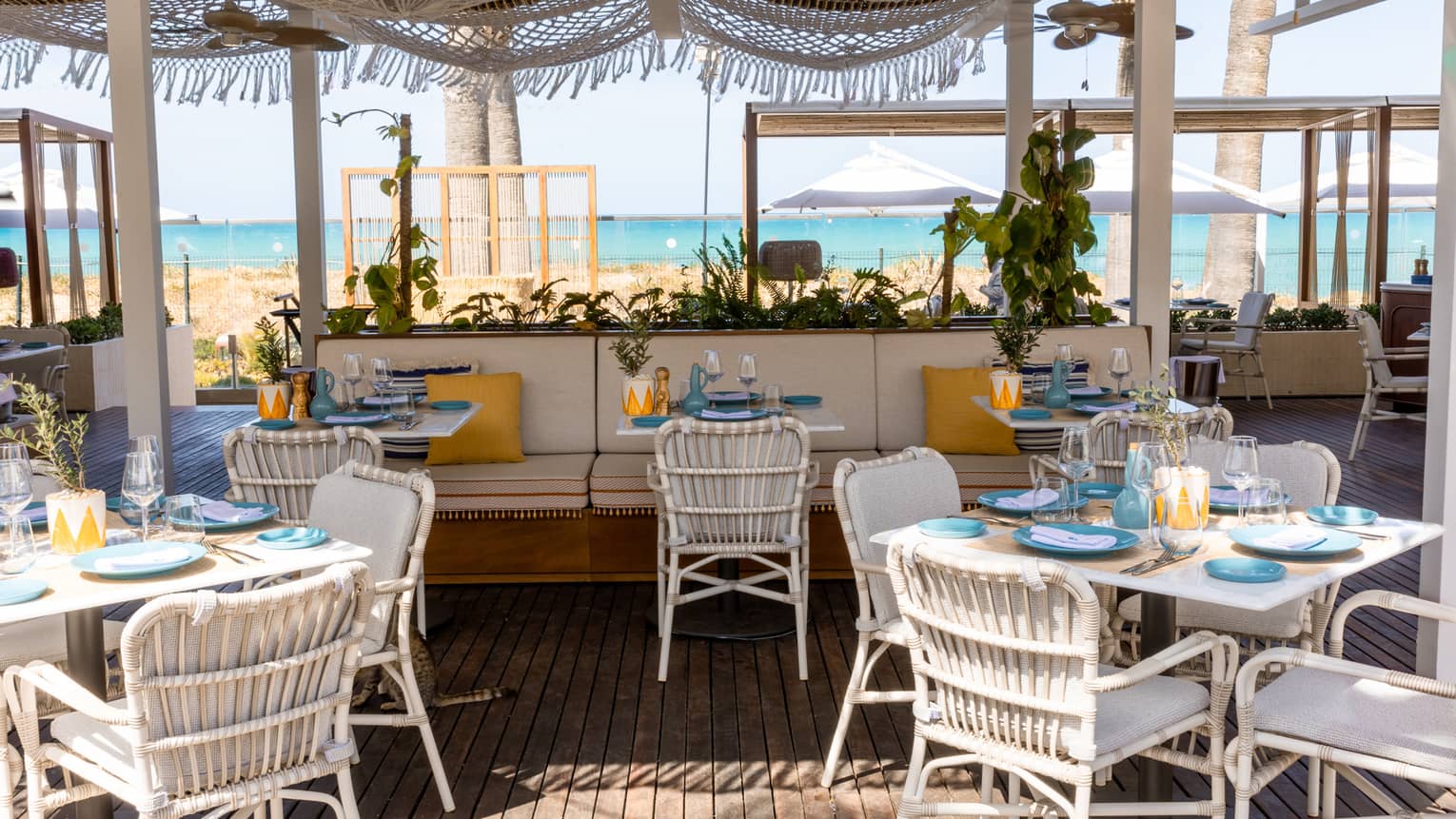 Restaurant terrace with white dining seating and banquettes with sea view in backdrop