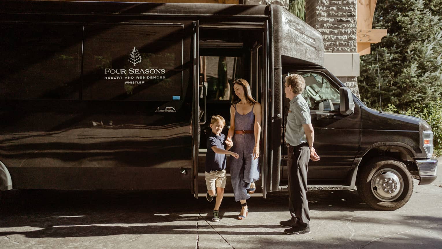 A family steps off of a black Four Seasons shuttle bus, underneath the shale stone entryway.