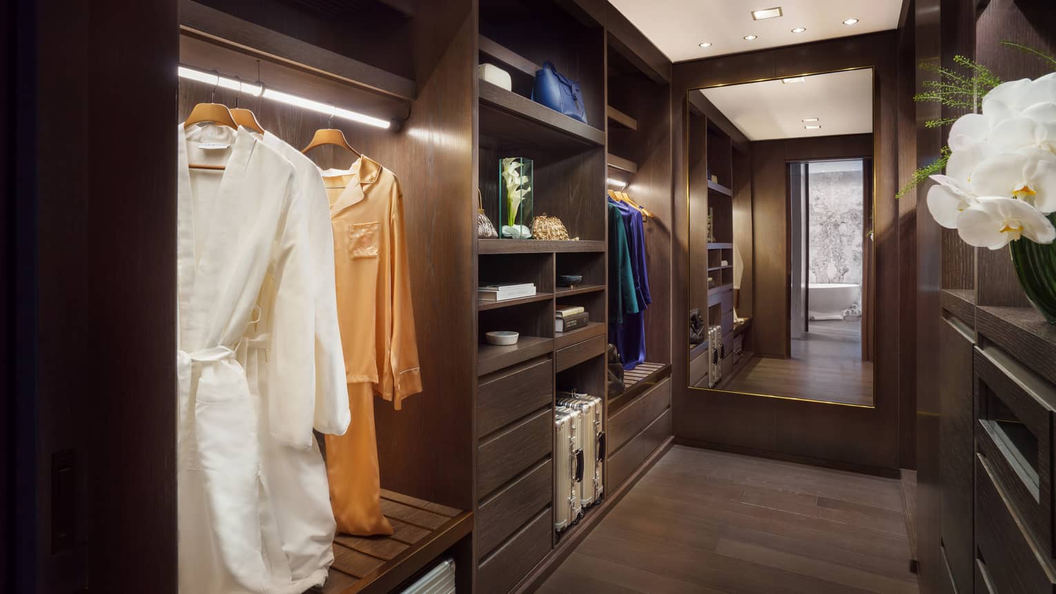 Large walk-in closet with built-in shelving, dark wood floors, floor length mirror