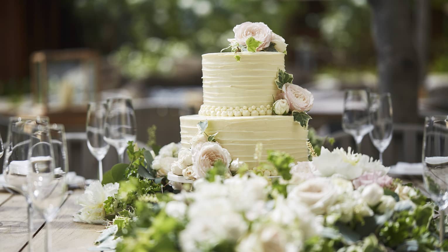 Two-tiered white wedding cake on banquet table with wine glasses, flowers