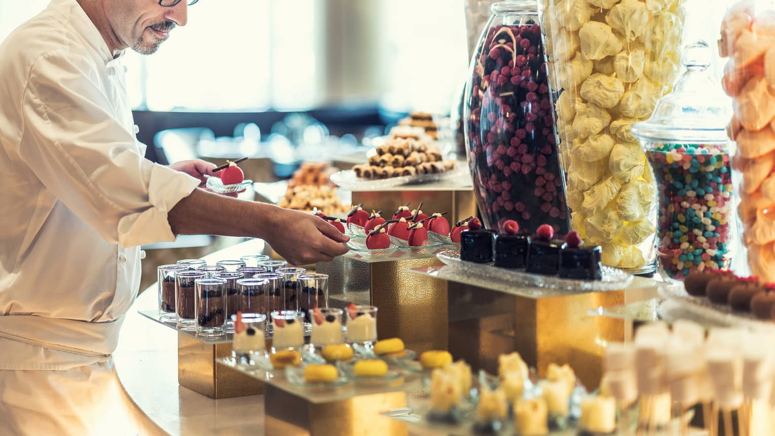 A chef prepares several chocolate pastries inside a patisserie. 