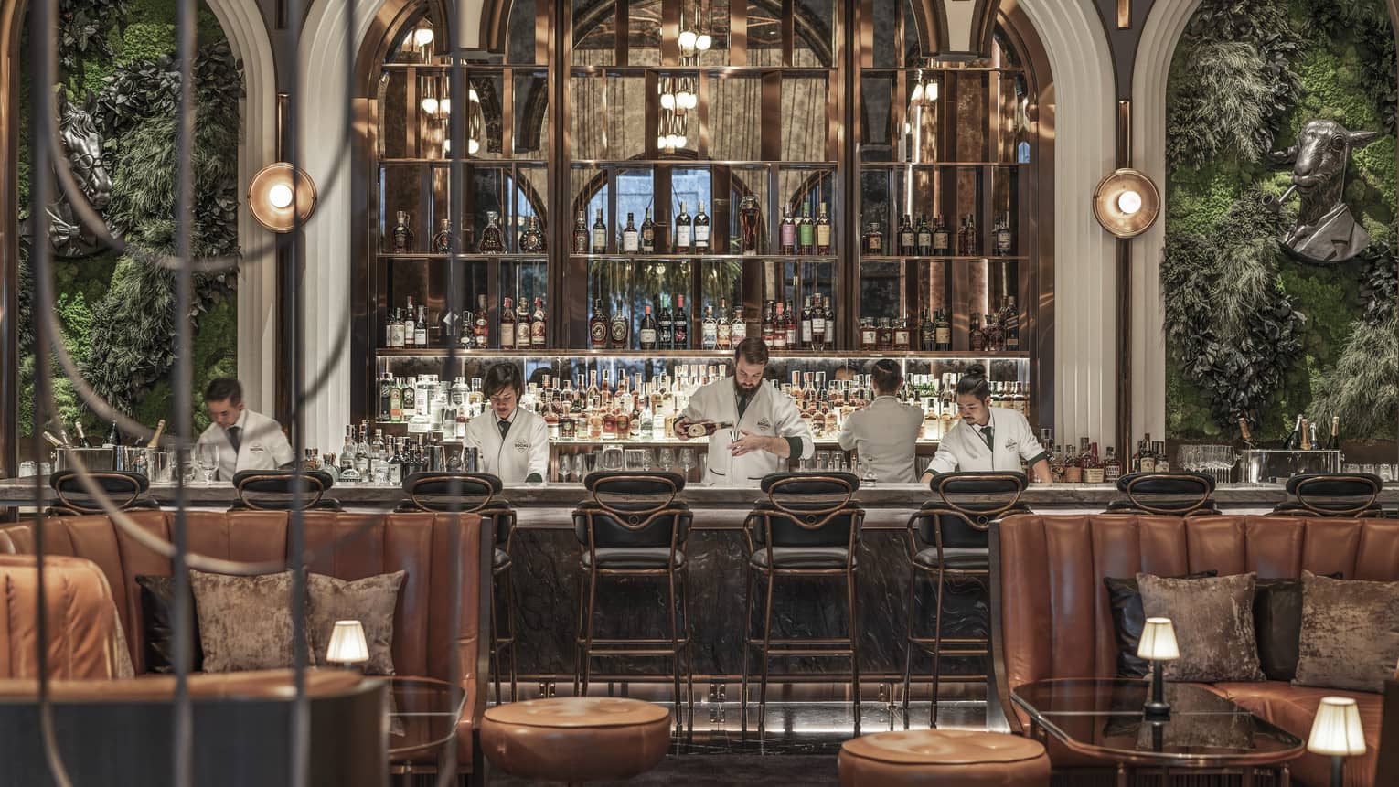 Five bartenders in white shirts prep behind a bar, brown leather booth seating in foreground