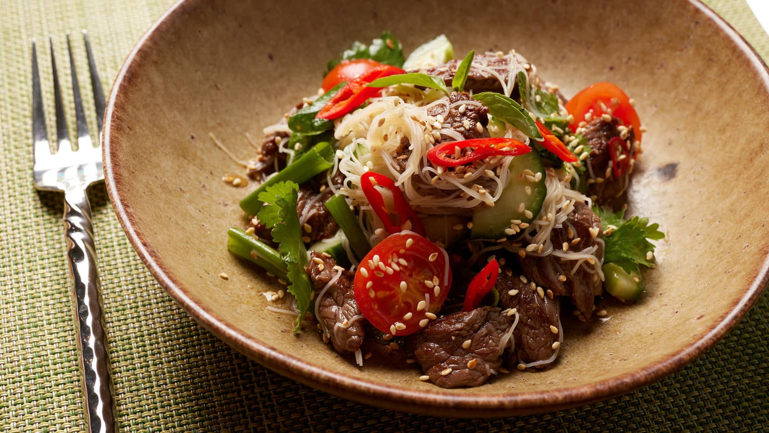 Sesame beef with sliced chillis, cilantro, scallions and ginger in brown bowl