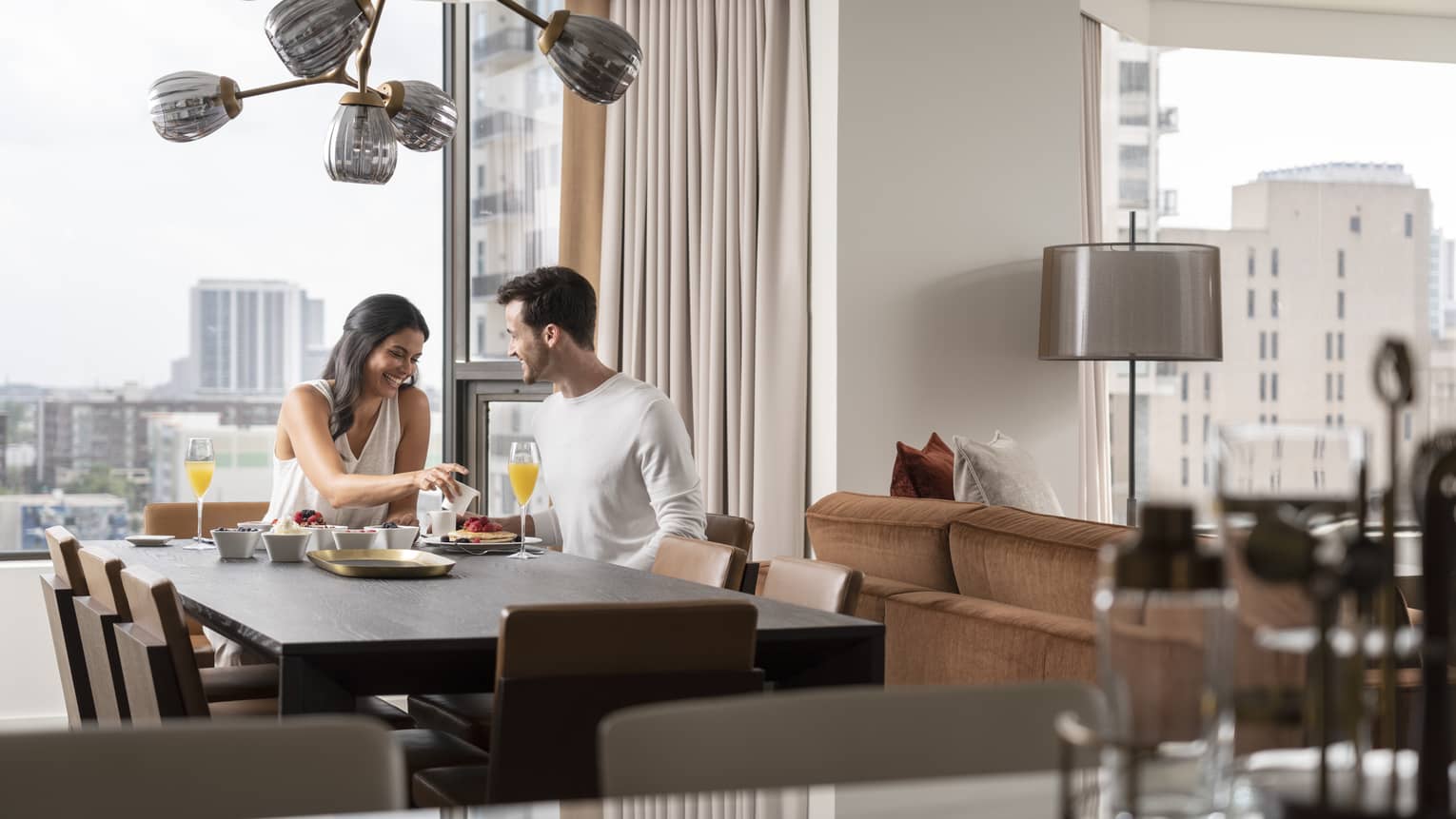 Smiling couple enjoys breakfast in their guest room, views of downtown Houston behind them 
