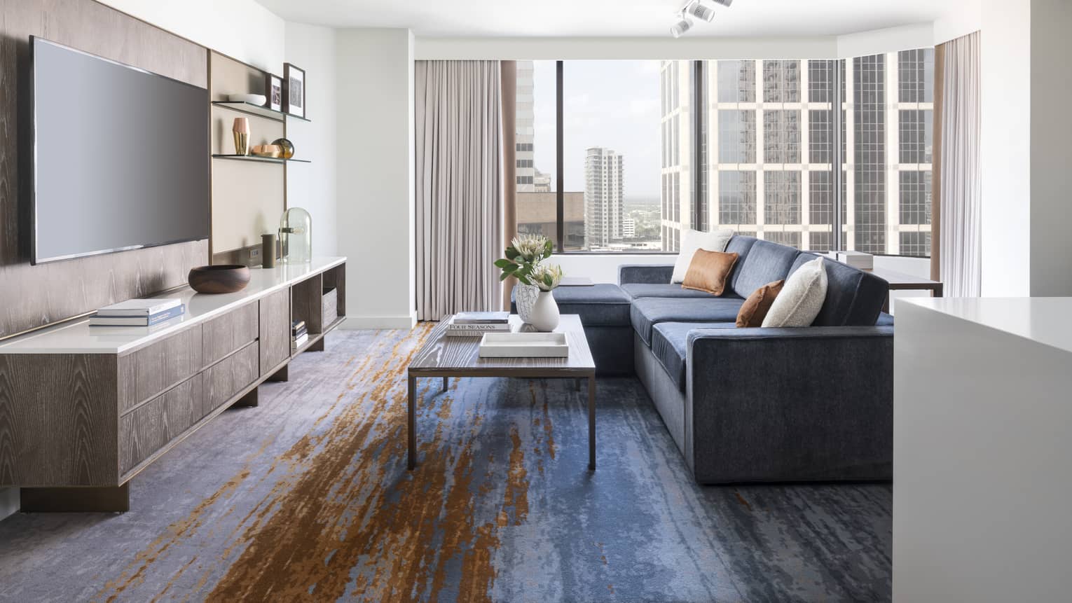 Two-bedroom Residential Suite living area with navy sectional sofa, floor-to-ceiling windows, city views