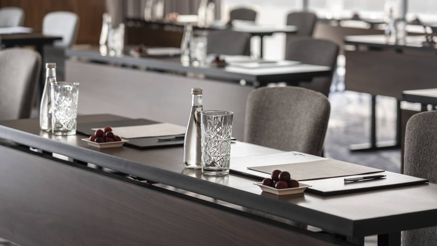 A close up of long desks with papers and water placed at each seat.