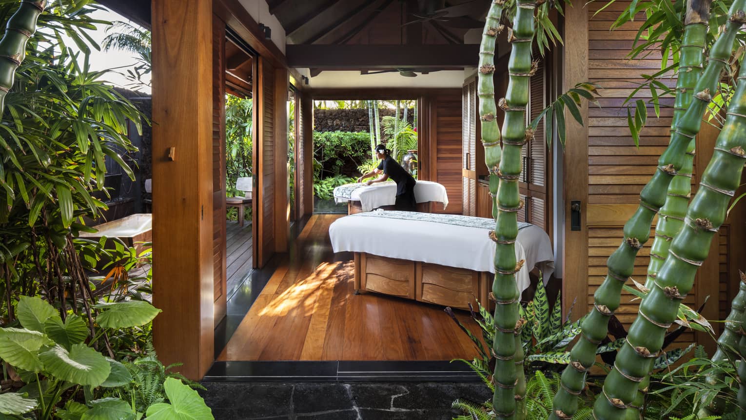 Spa staff spreads sheet on couples massage beds on open-air pavilion 