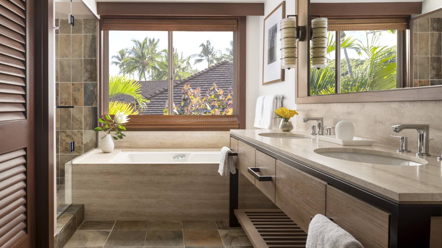 Bathroom with tub underneath large window, earth-tone tile floors, double vanity