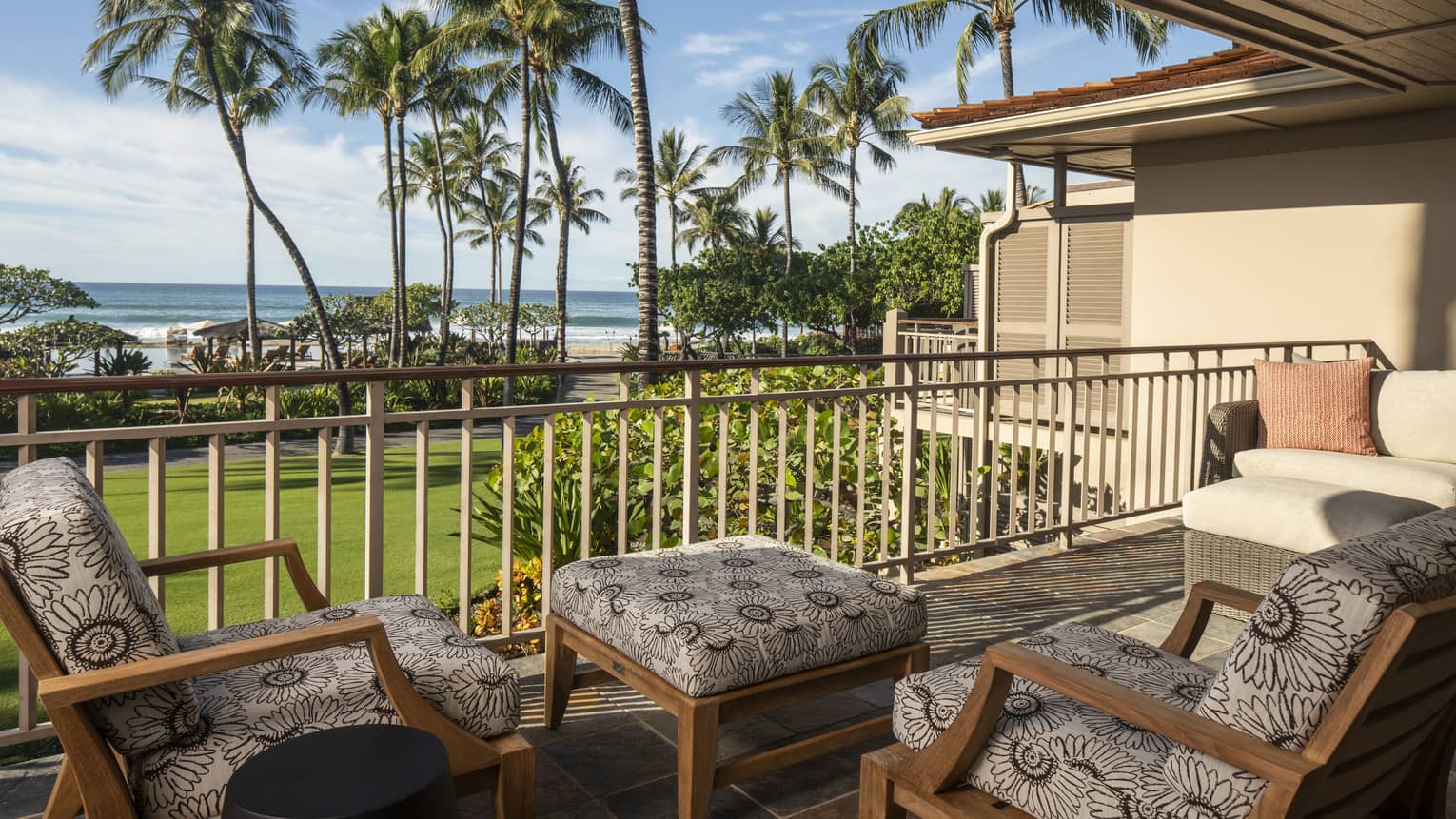 Outdoor balcony with two cushioned chairs and matching ottoman, view of lawn, palm trees and ocean