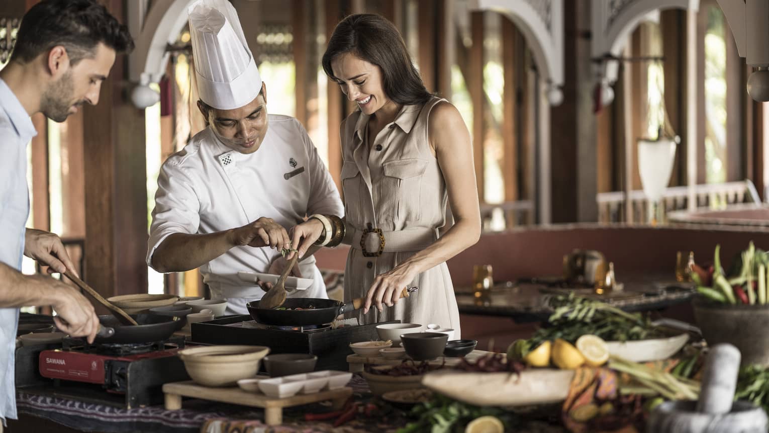 A chef doing an interactive cooking lesson with a man and a woman at the Four Seasons Langkawi
