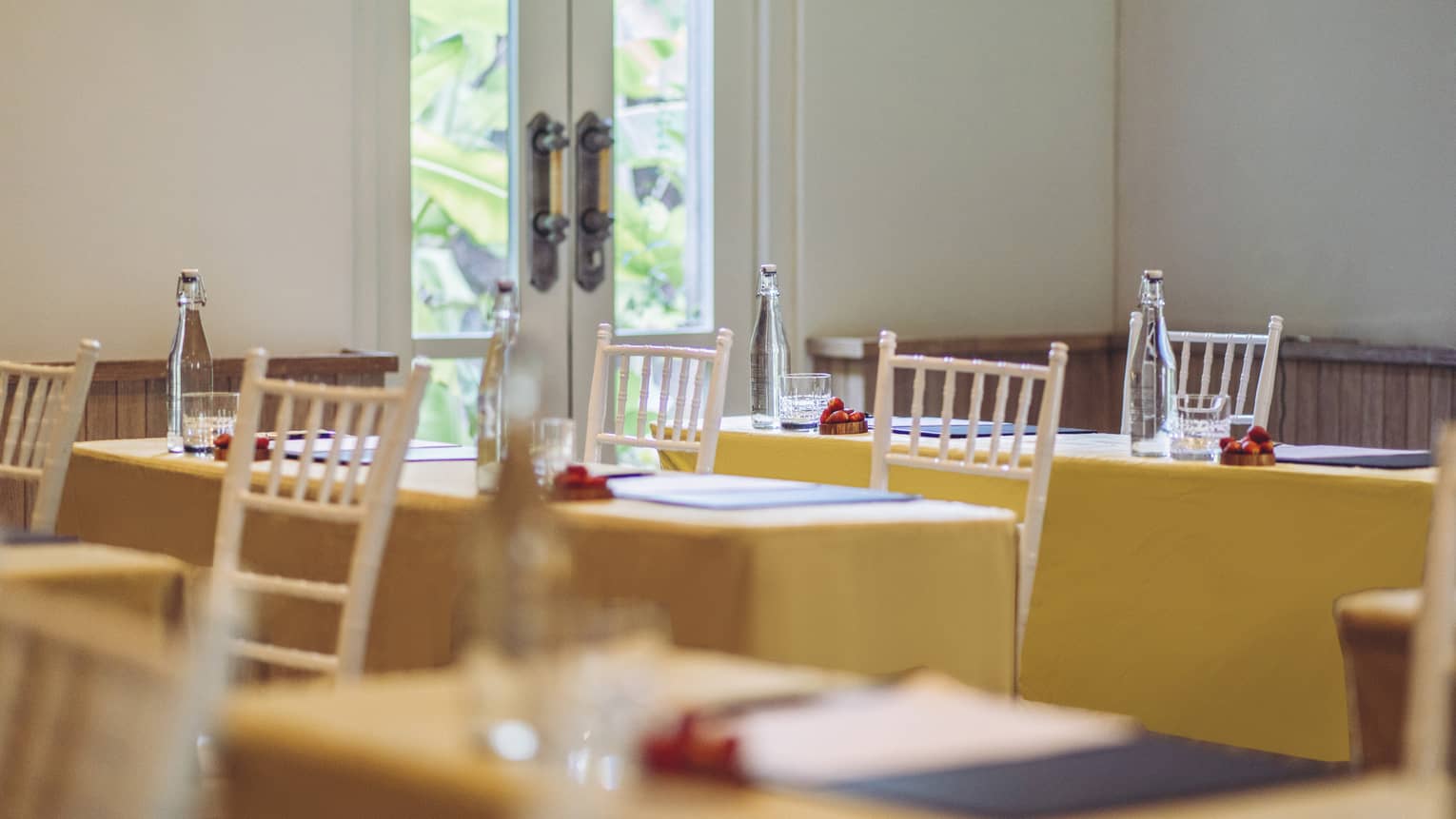Tables with two white chairs, each with yellow table clothes, set for meeting