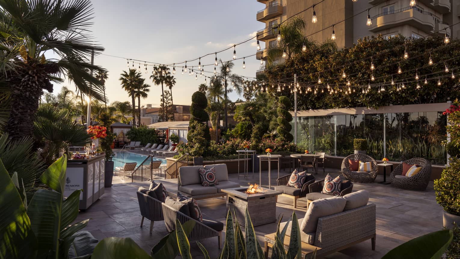 An outdoor seating area with fairy lights next to a pool and palm trees.