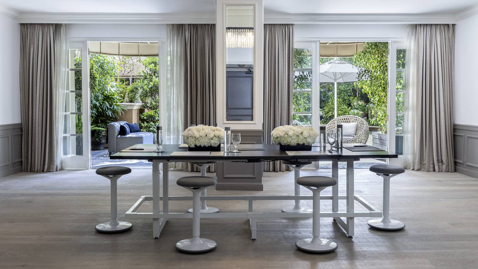 A meetings room with a large table surrounded by stools and large open windows in the background.