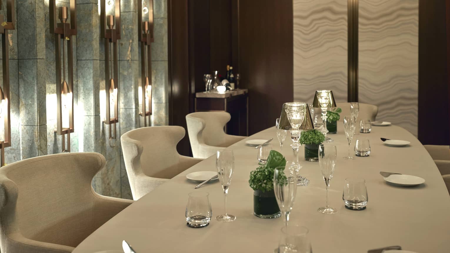 Rectangular table set for eight with white linens and minimal green centerpieces, lighted wall sconces to the left