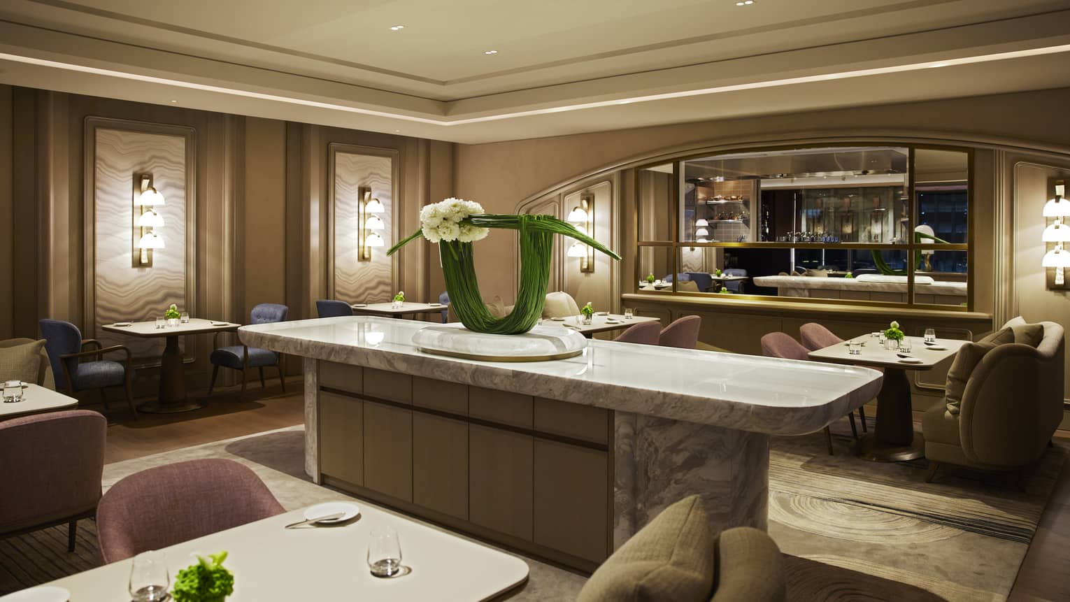 Dimly lit dining area with beige and blush tones, lighted wall sconces, marbled centre island