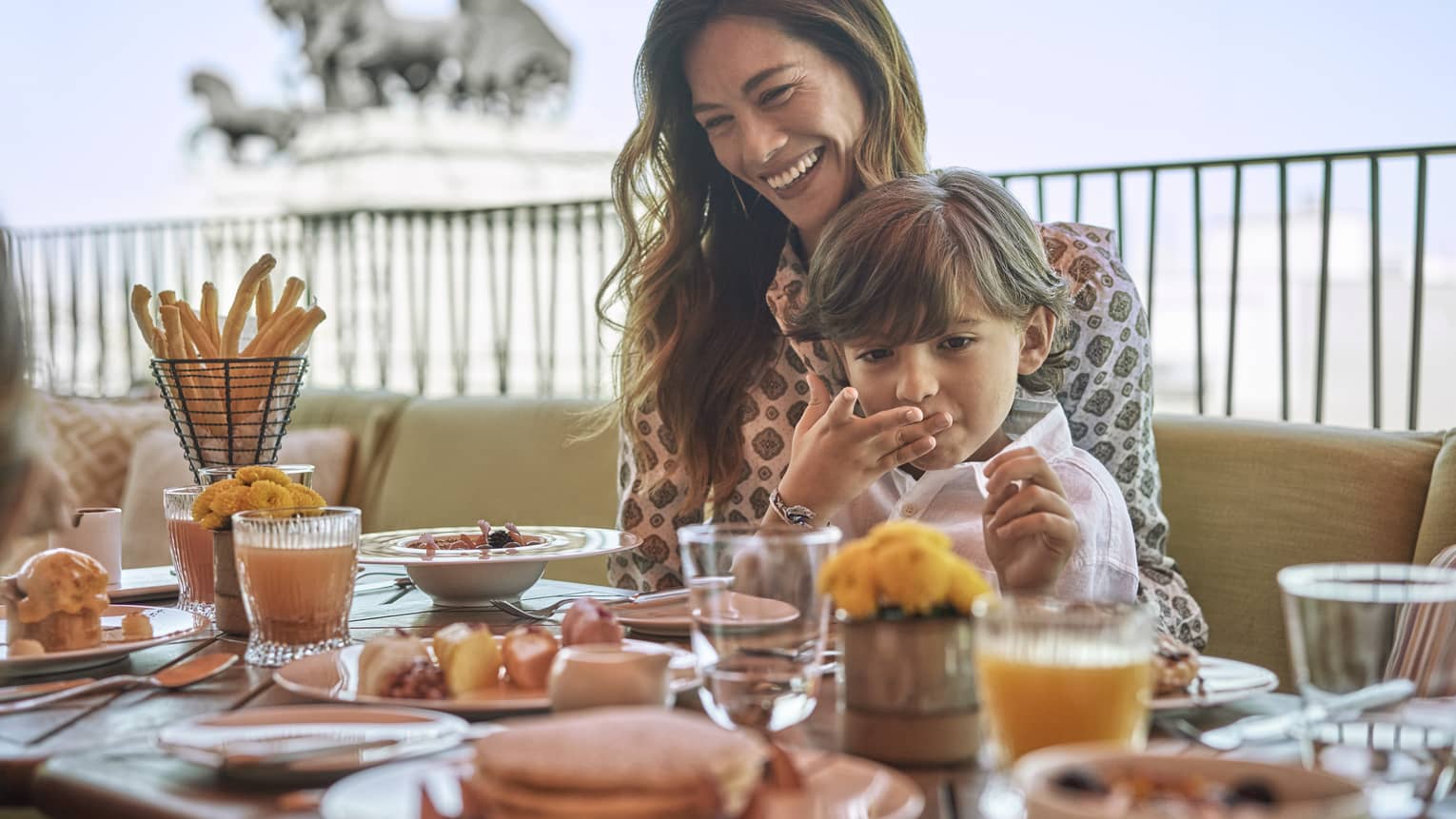 Woman and young boy sit at outdoor restaurant table with food