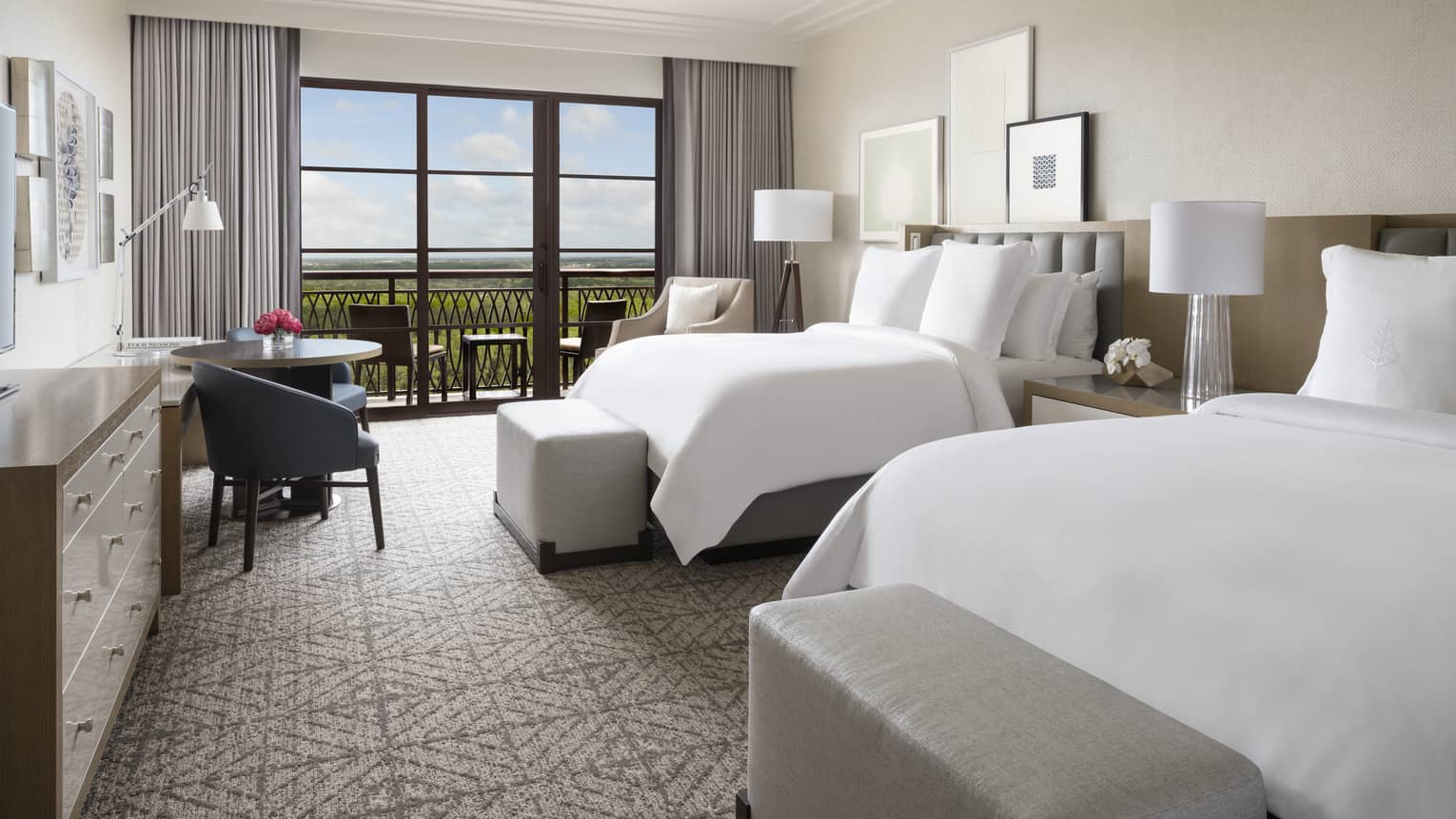 Hotel room with two double beds, small table and black chair, walk-out balcony