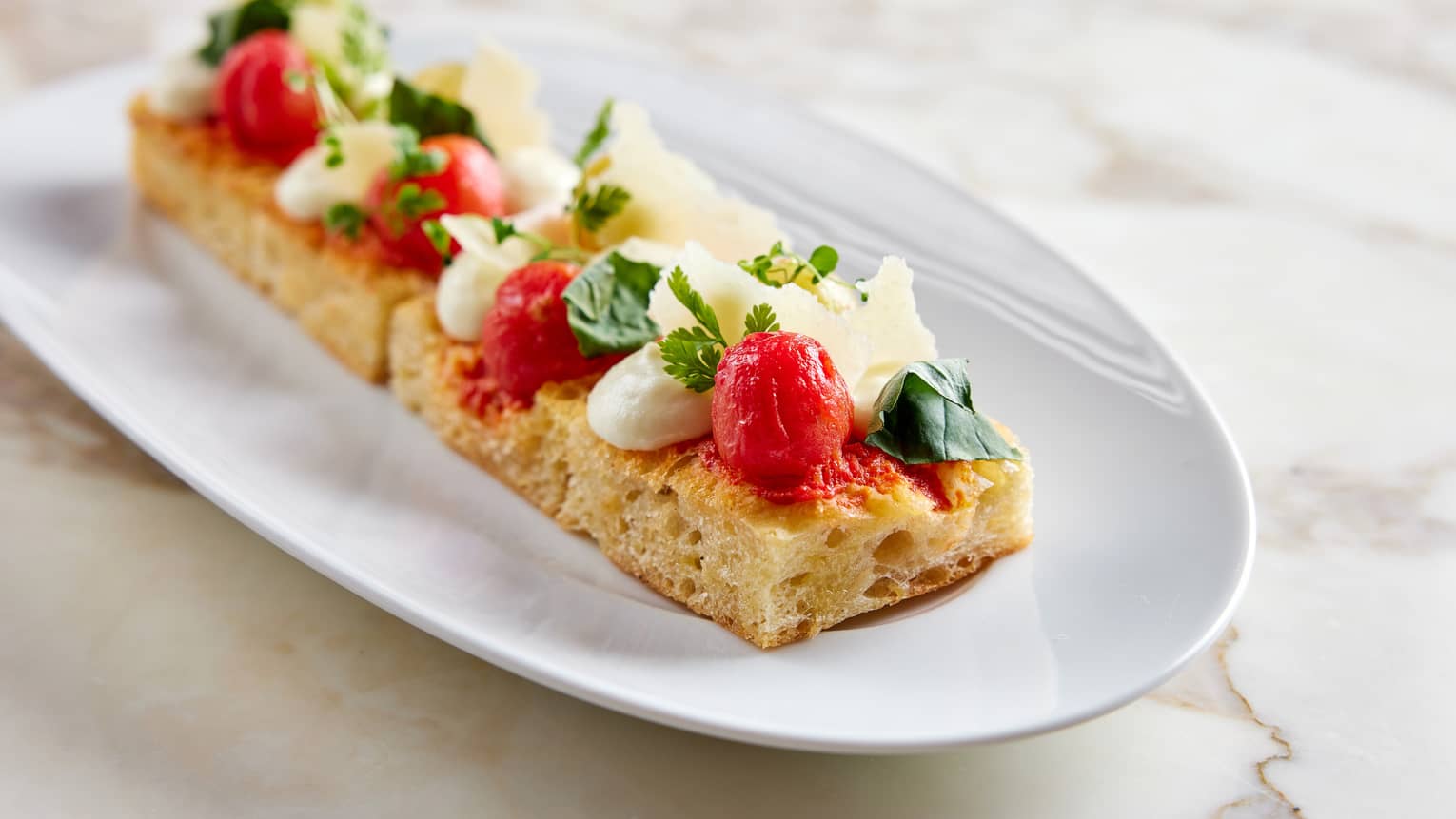 Rectangular Foccacia Topped withWhipped Mozzarella, Marinated Tomato, Basil on white oval dish