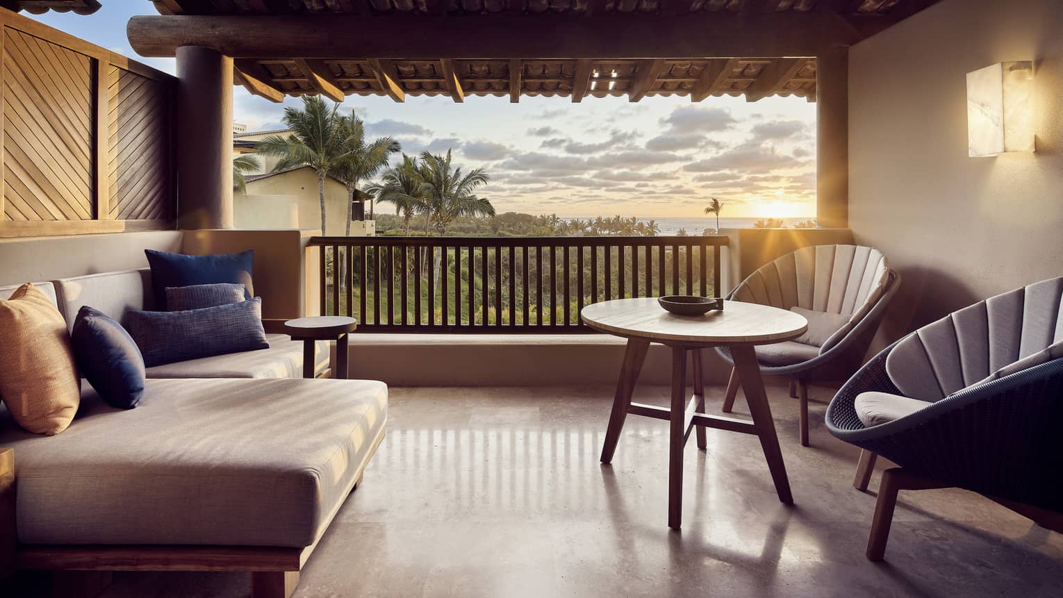 A sunlit hotel balcony with two chairs, a small table, and a sofa.
