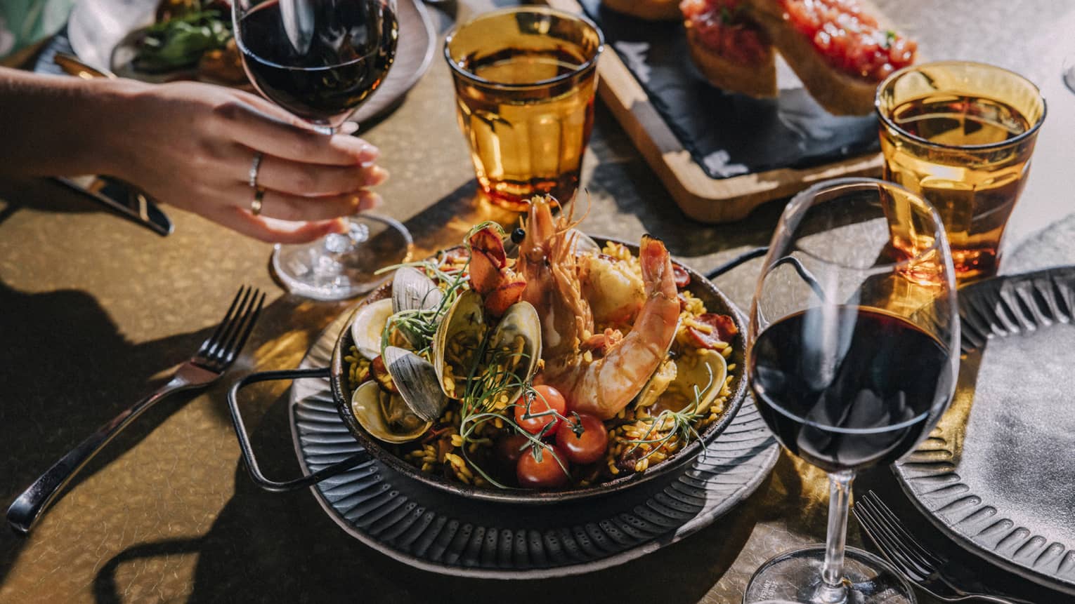Paella dish on a table with glass of water and red wine