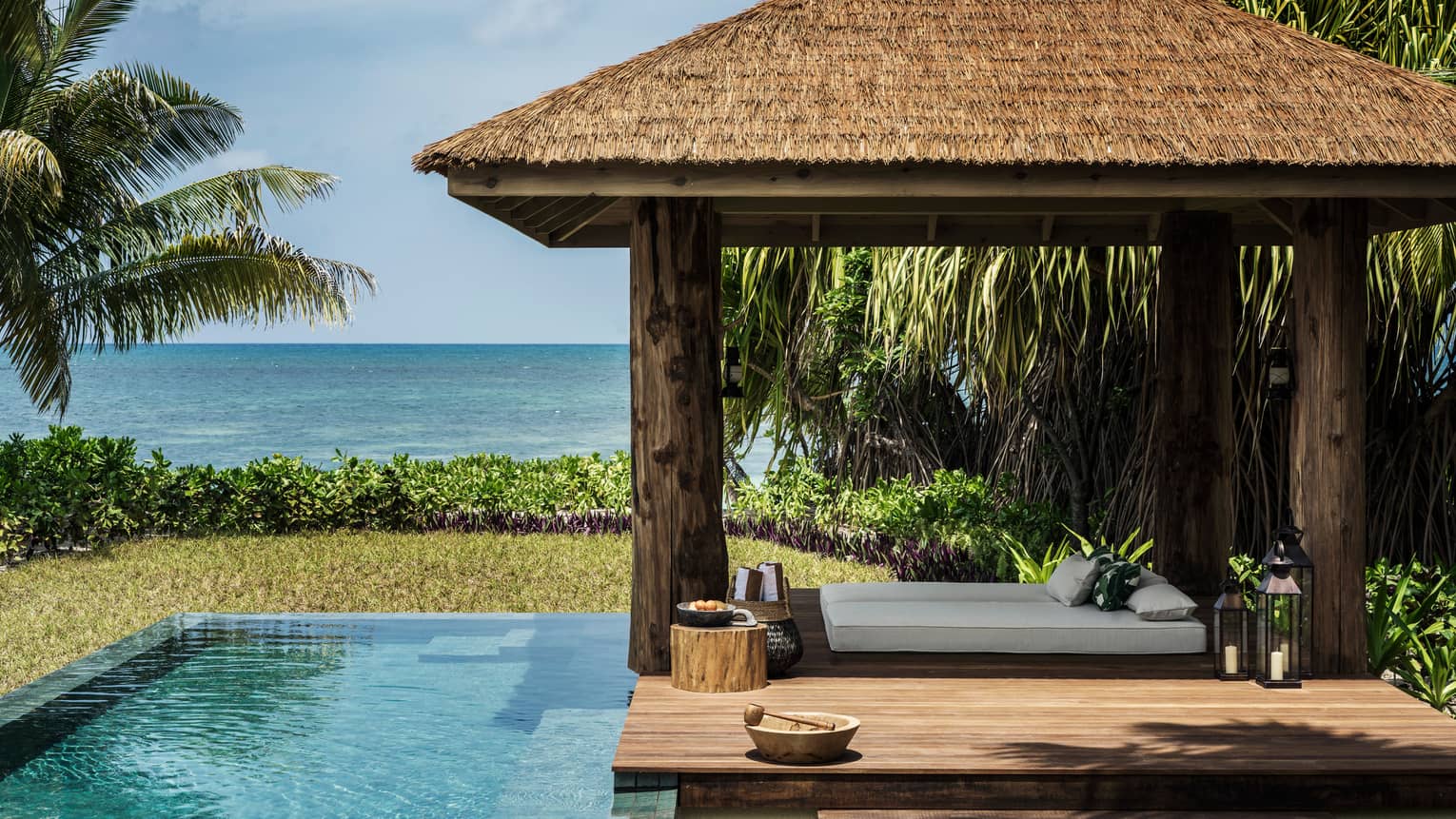 Four-pillar wooden cabana and infinity edge pool, sea in the distance